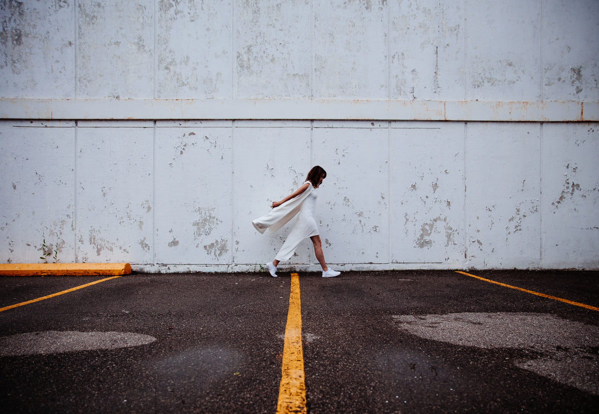 All-white monochrome outfit with a woman in a white dress and sneakers walking outdoors