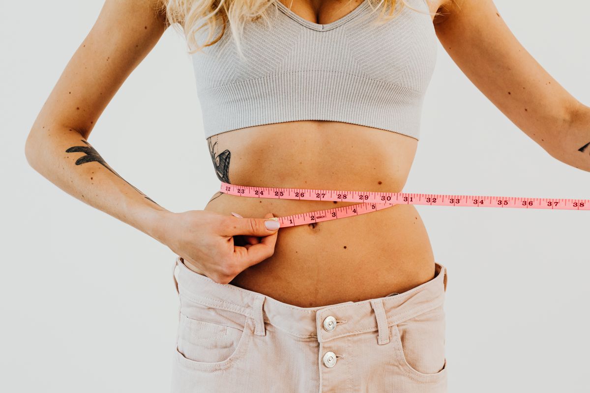 Plus size size guide with a woman measuring her waist with a pink tape measure